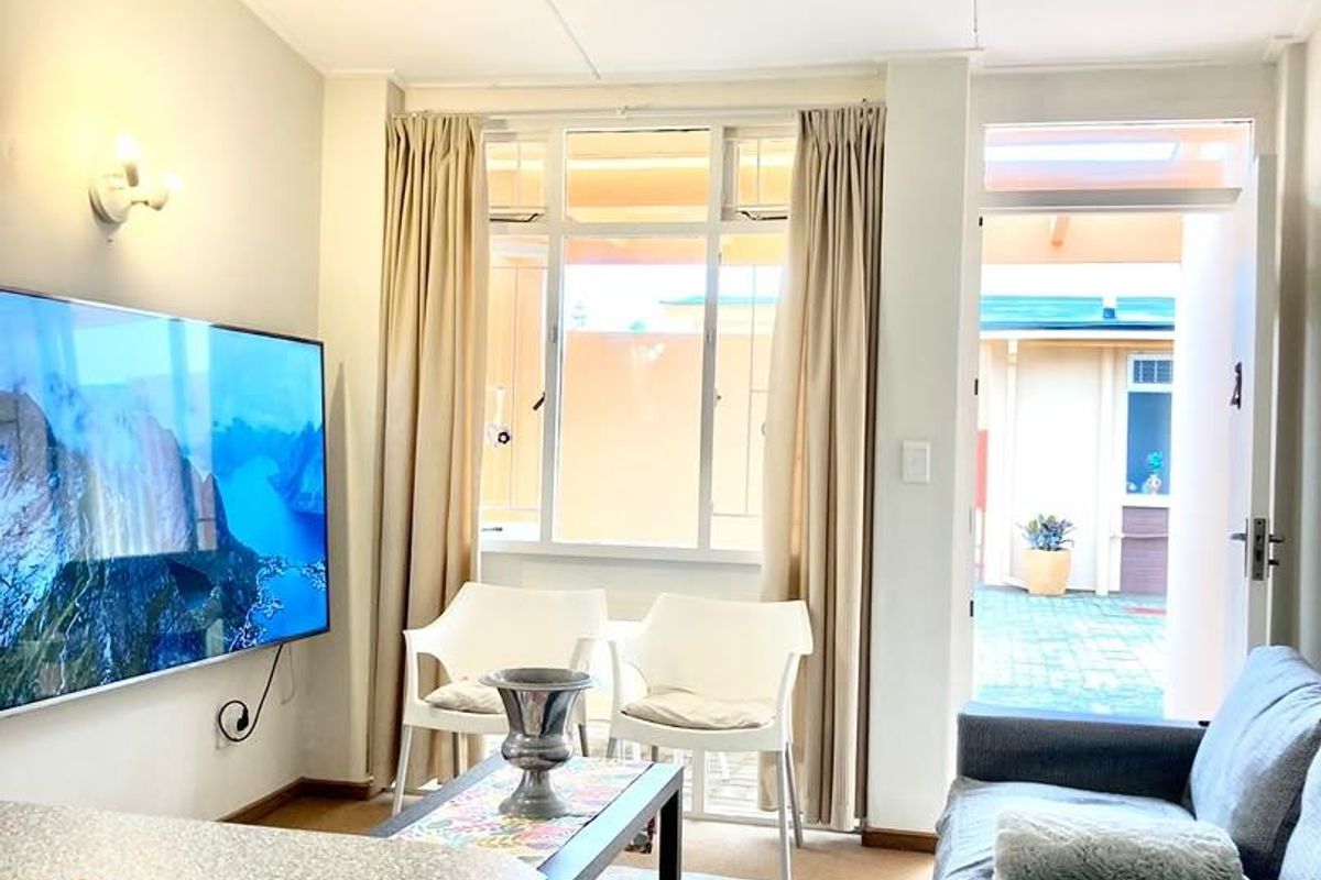 A bright living room featuring a large window, wall-mounted lighting, and direct access to an outdoor patio area.