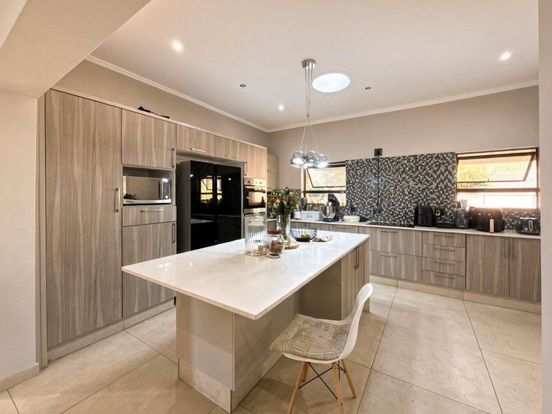 Modern kitchen featuring a central island with stone countertops, sleek wood-grain cabinetry, built-in appliances, mosaic tile backsplash, and a skylight for natural light.