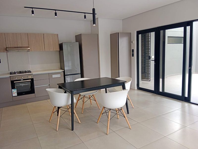 Modern open-plan kitchen and dining area featuring sleek cabinetry, integrated appliances, tiled flooring, and direct access to an outdoor patio through sliding glass doors.