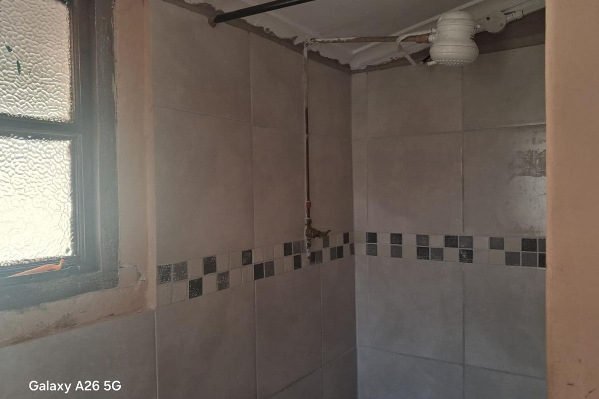 A bathroom shower area featuring tiled walls and an electric shower unit, currently requiring renovation and finishing of the surrounding wall surfaces.