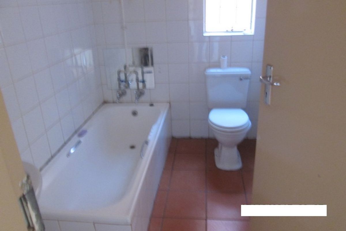 A dated bathroom featuring a standard bathtub, toilet, and tiled finishes, offering a blank canvas for potential renovation and modernization.