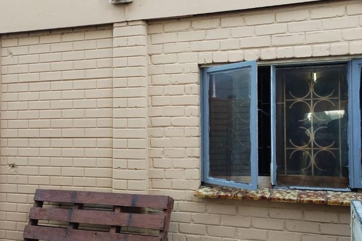 A view of the rear exterior brick wall featuring a casement window with security bars and a concrete sill.