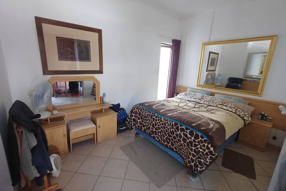 A bedroom featuring tiled flooring, a built-in headboard, and a large wall-mounted mirror.