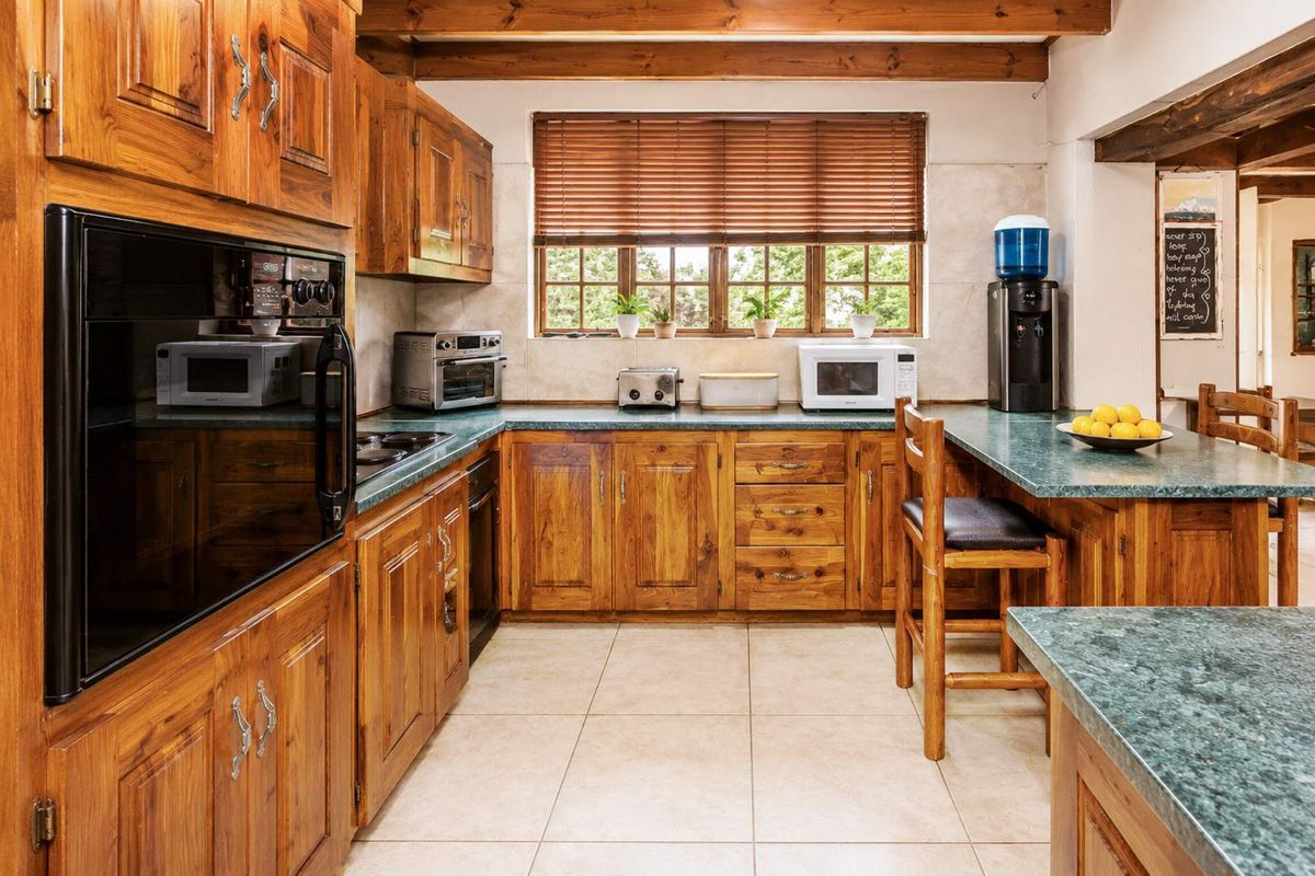 A traditional kitchen featuring extensive wooden cabinetry, exposed ceiling beams, tiled flooring, and a functional layout with integrated oven and cooktop.