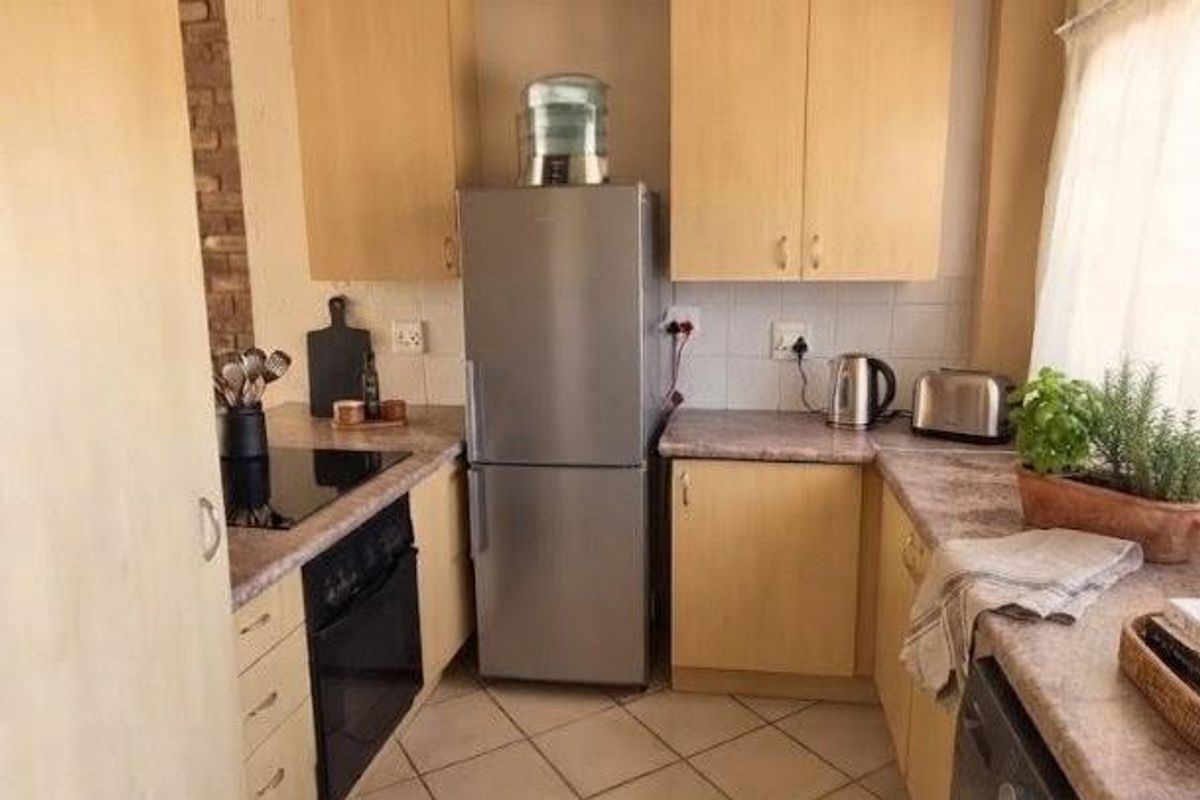A functional kitchen featuring light wood-finish cabinetry, laminate countertops, tiled flooring, and integrated appliances including an oven and hob.