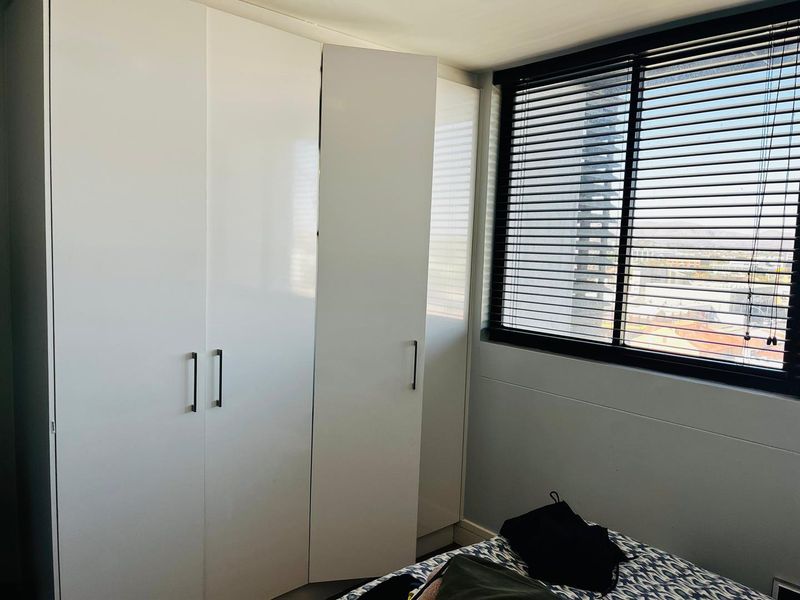 A bedroom featuring modern white built-in wardrobes and venetian blinds, offering a clean and functional storage solution.