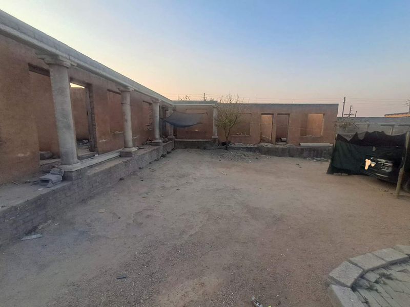 An unfinished rear courtyard area featuring stone columns and exposed brick structure, requiring significant completion and landscaping to reach its full potential.