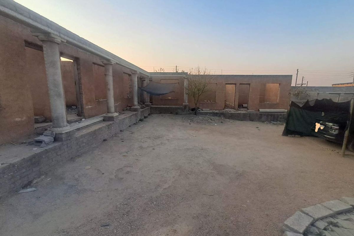 An unfinished rear courtyard area featuring stone columns and exposed brick structure, requiring significant completion and landscaping to reach its full potential.