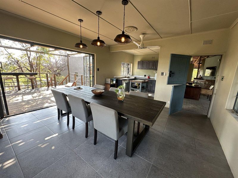 Spacious open-plan dining and kitchen area featuring modern tiled floors, pendant lighting, and seamless access to an outdoor wooden deck.