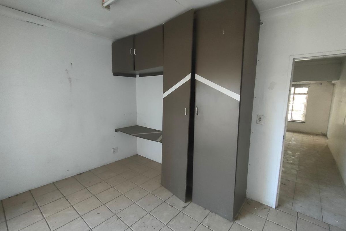 A bedroom featuring built-in cupboards and a desk area with tiled flooring, requiring cosmetic updates and repairs.