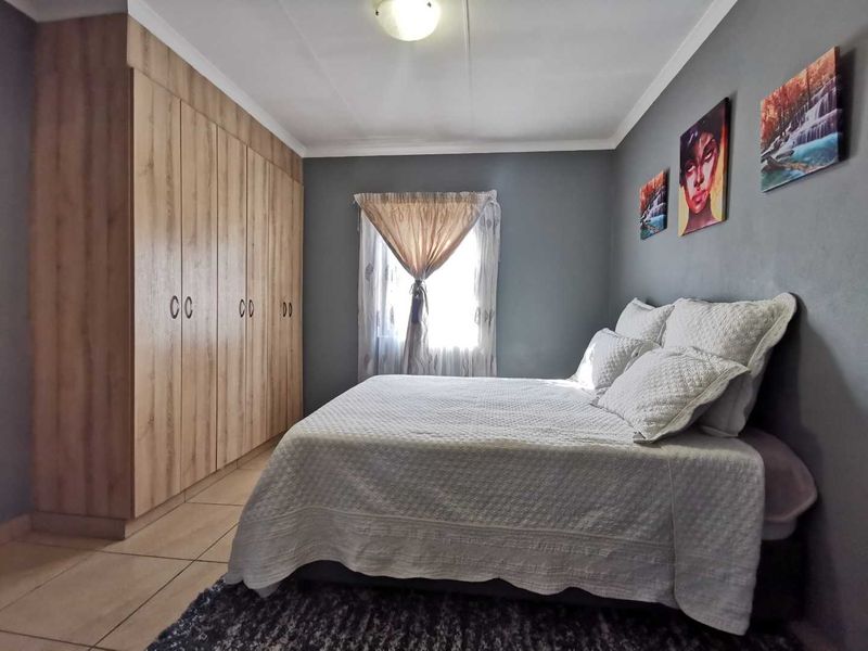 A well-maintained bedroom featuring light wood-finish built-in cupboards, neutral grey walls, and tiled flooring.