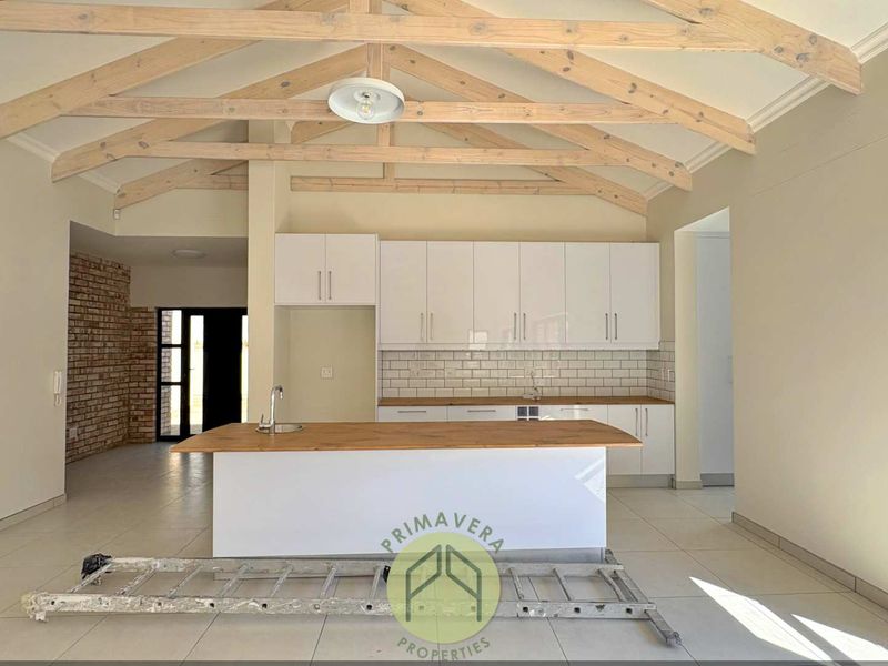 Modern kitchen featuring exposed timber roof trusses, a central island with sink, white cabinetry, and subway tile backsplash in an open-plan layout.