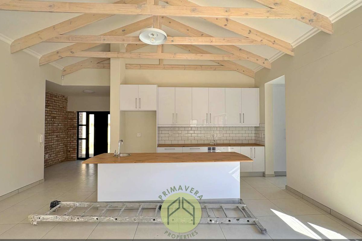 Modern kitchen featuring exposed timber roof trusses, a central island with sink, white cabinetry, and subway tile backsplash in an open-plan layout.