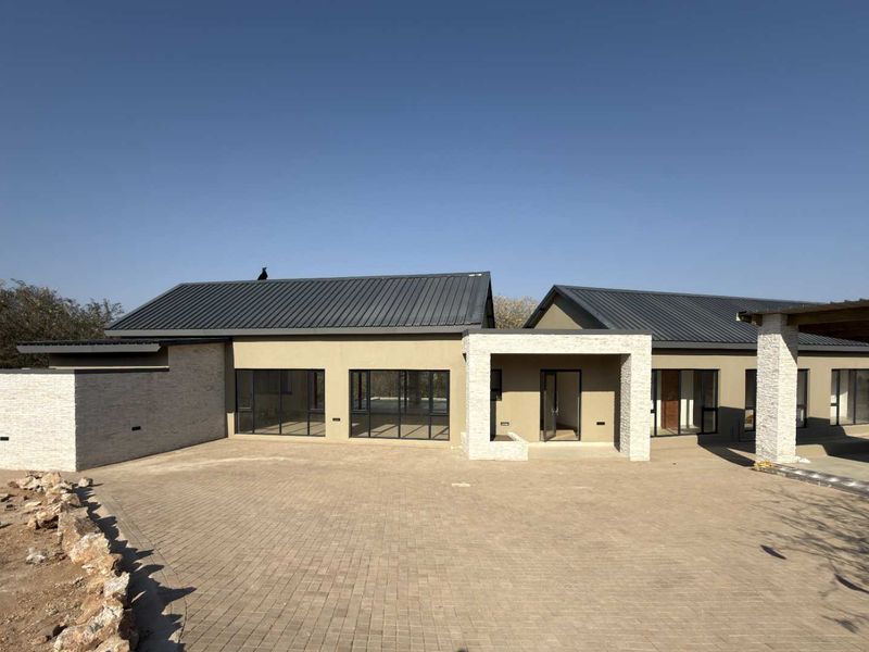 Modern single-story residence featuring a paved driveway, stone cladding accents, and dark metal roofing, presenting a contemporary architectural facade.
