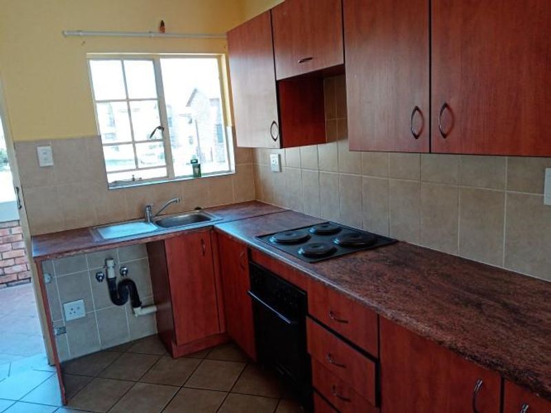 A functional kitchen featuring wooden cabinetry, laminate countertops, a built-in oven and hob, and tiled finishes throughout.