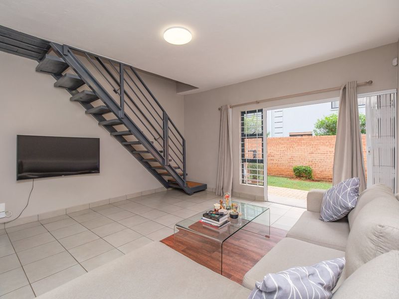Open-plan living area featuring a modern metal staircase, tiled flooring, and direct access to a private rear garden through sliding glass doors.