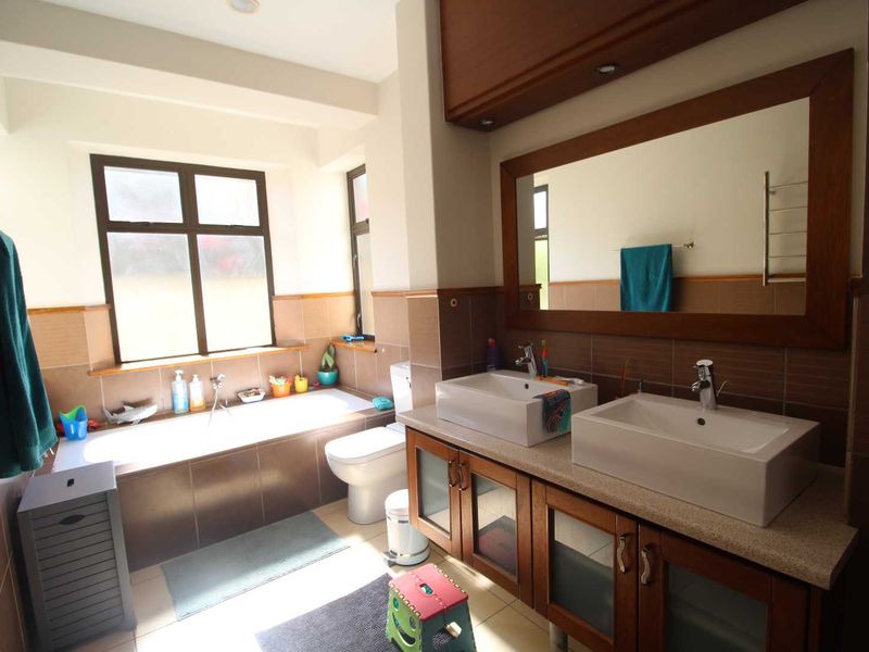 A well-maintained bathroom featuring a double vanity with vessel sinks, a built-in bathtub, and large wall-mounted mirror with wood framing.