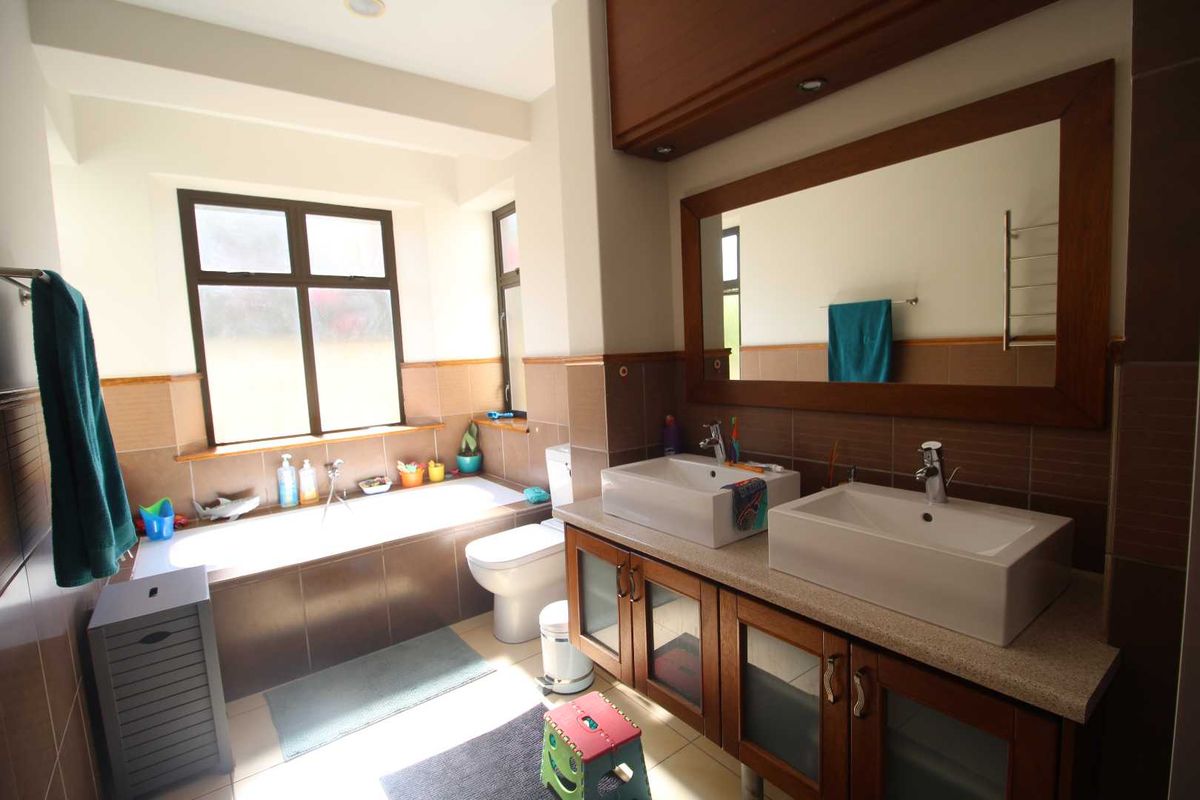 A well-maintained bathroom featuring a double vanity with vessel sinks, a built-in bathtub, and large wall-mounted mirror with wood framing.