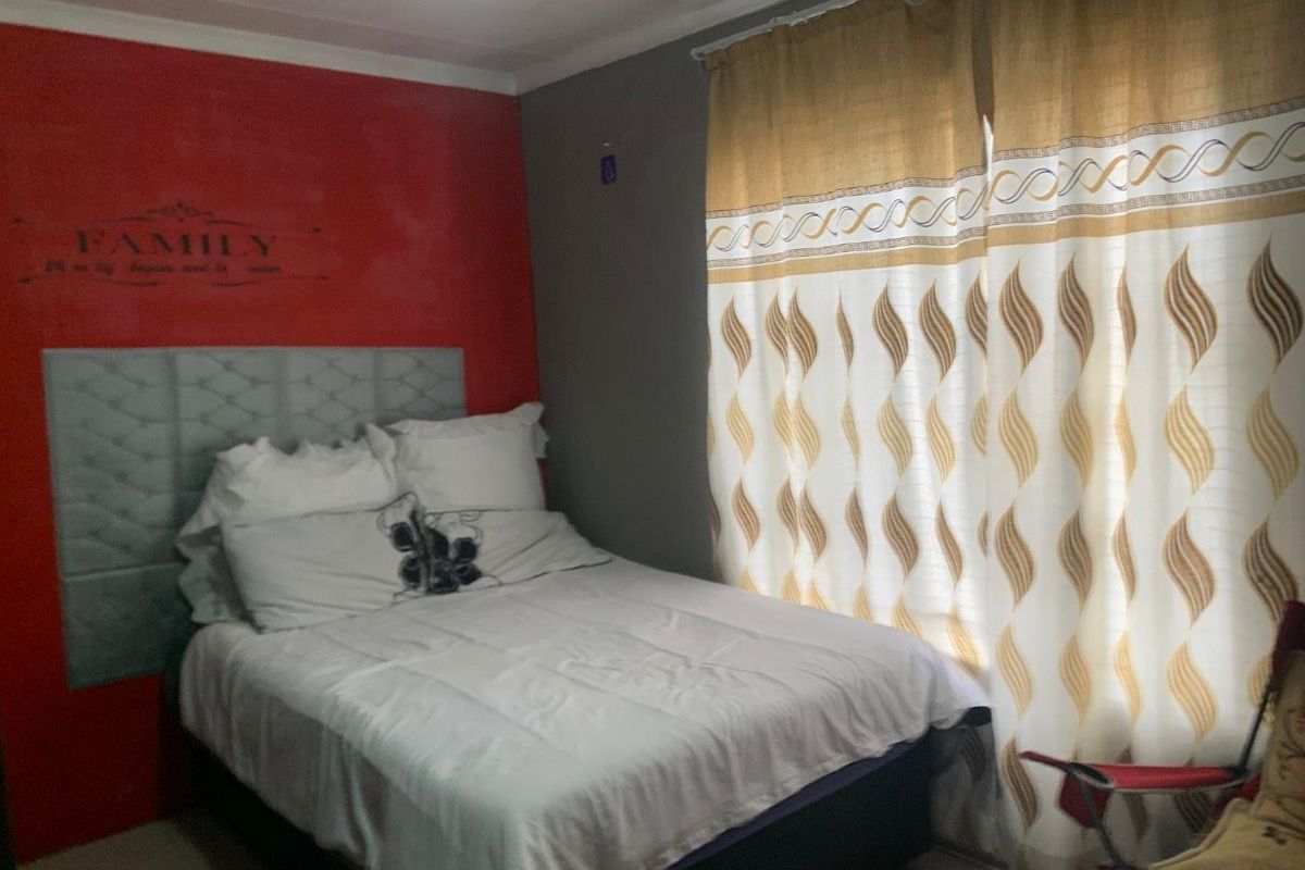 A bedroom featuring a red accent wall and neutral grey walls, complemented by floor-to-ceiling curtains.