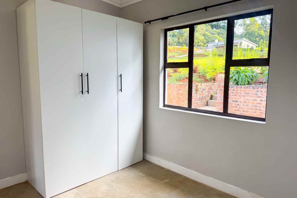 A bright bedroom featuring neutral walls, a large built-in wardrobe, and a window overlooking the garden.