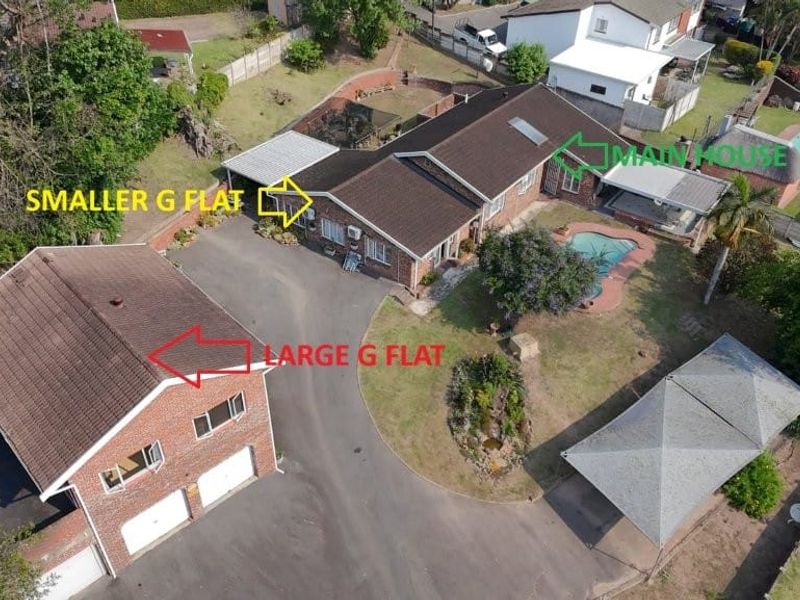 Aerial view of a residential property featuring a main house, two separate flatlets, a swimming pool, and a paved driveway with carport.