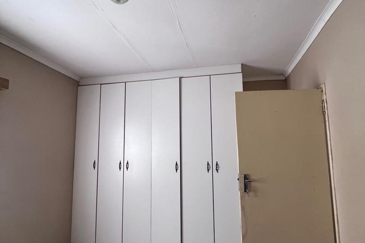 A vacant bedroom featuring built-in white cupboards, tiled flooring, and a standard ceiling light fixture, ready for a modern update.