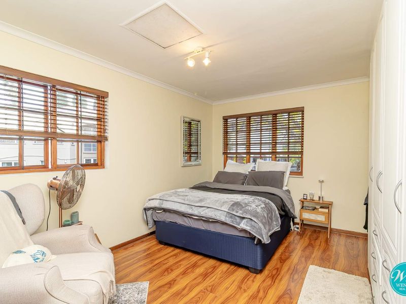 A well-maintained bedroom featuring timber laminate flooring, built-in wardrobes, and dual windows with timber venetian blinds, providing a bright and functional living space.