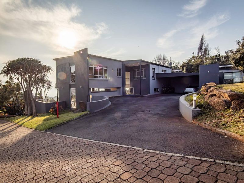 Modern multi-level residential property featuring a paved driveway, covered carport, and landscaped retaining walls with exterior lighting.
