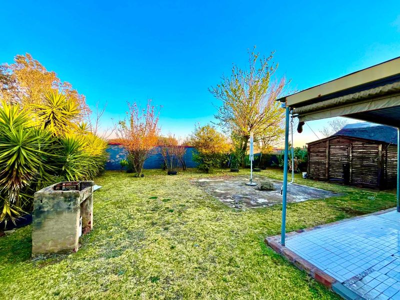 A spacious rear garden featuring a covered patio, a built-in brick barbecue, and a wooden storage shed, offering potential for outdoor landscaping and improvement.