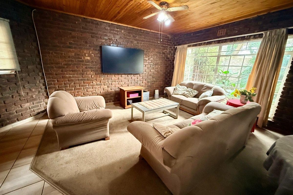 A cozy living room featuring exposed brick walls, a timber-paneled ceiling with a central fan, and large windows providing natural light.