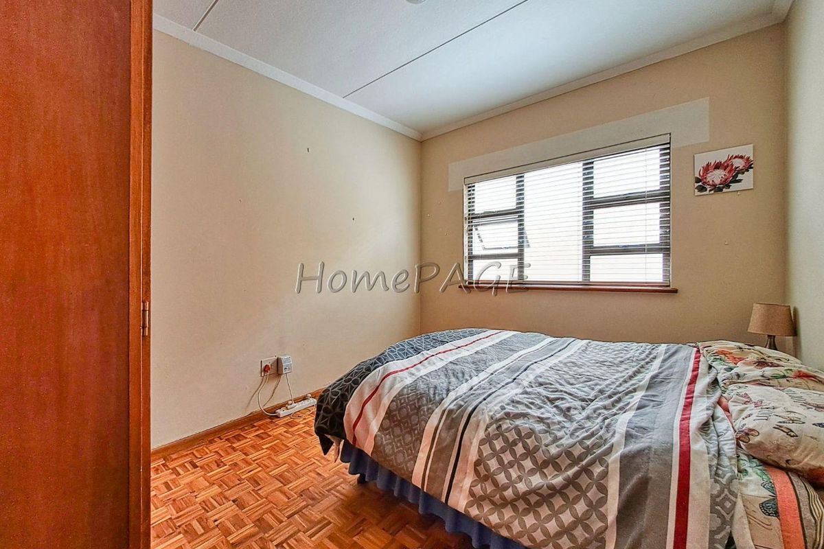 A bedroom featuring parquet flooring, a window with fitted blinds, and neutral wall finishes.