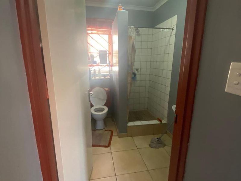 A functional bathroom featuring a shower cubicle, toilet, and tiled flooring, requiring cosmetic updates to modernize the space.