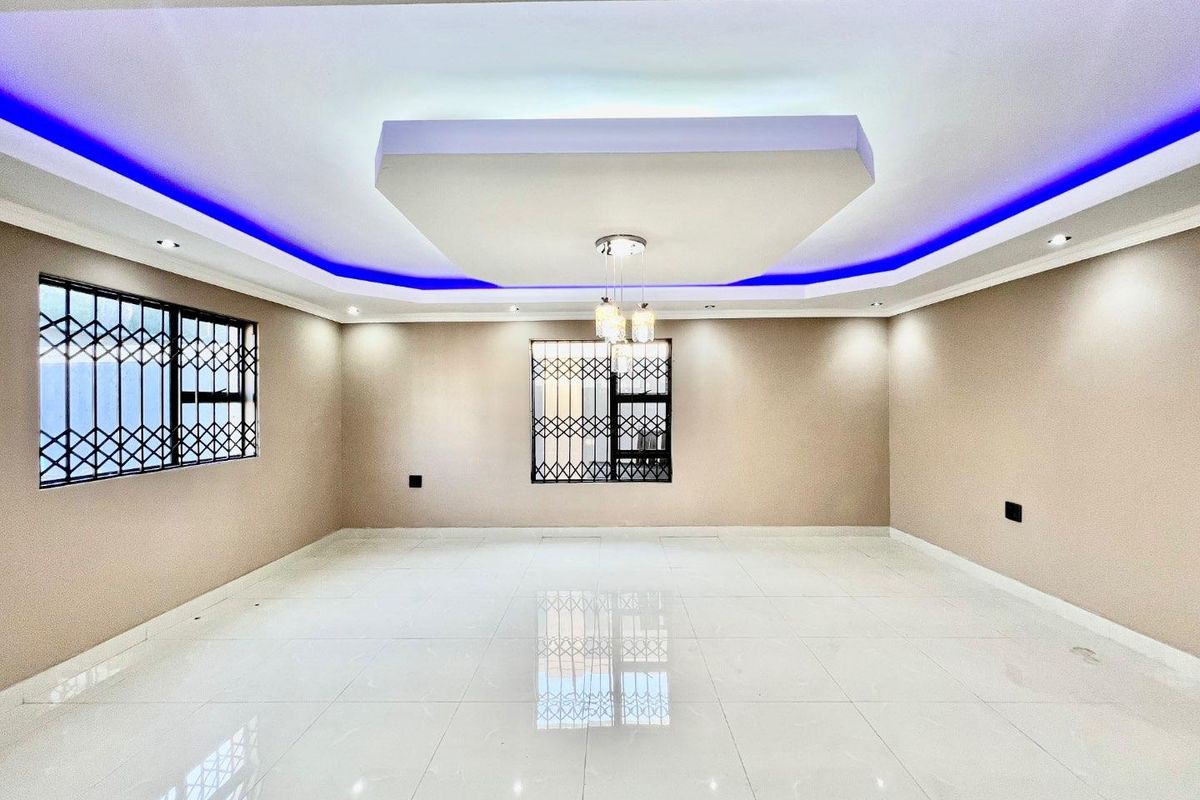 Spacious, empty living area featuring polished tiled floors, a modern recessed ceiling with integrated LED lighting, and secure window bars.