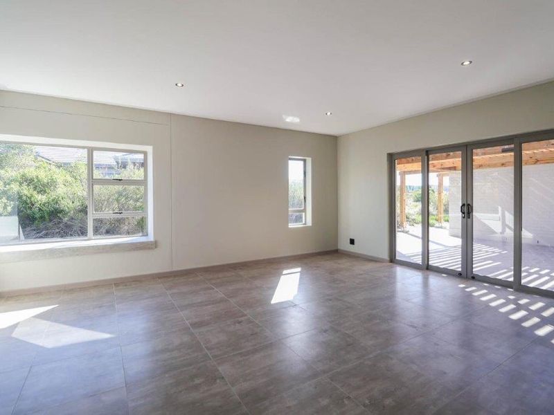Spacious, light-filled living area featuring large format floor tiles, recessed downlighting, and seamless access to an outdoor patio through aluminium sliding doors.