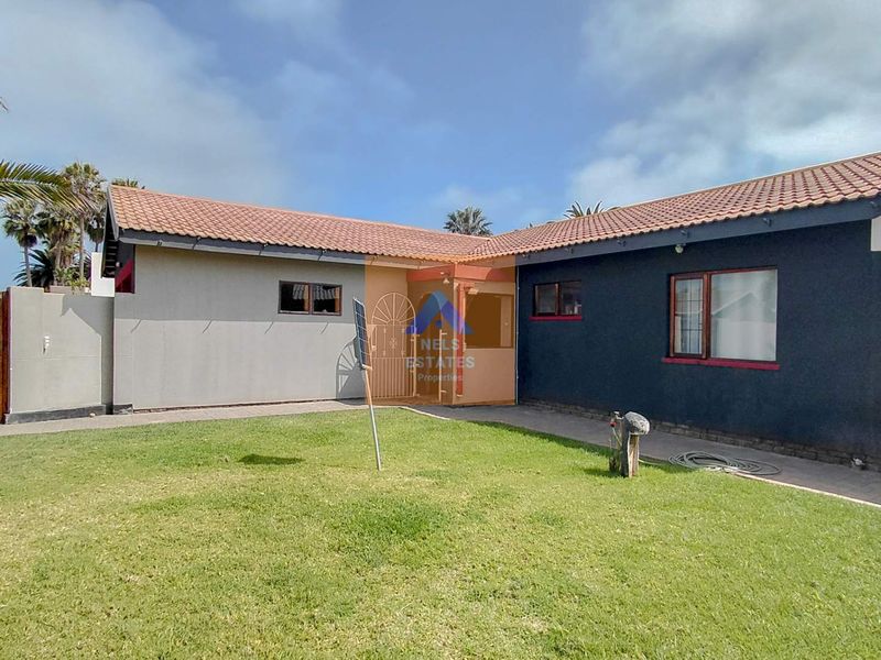 A rear view of the house featuring a tiled roof, paved walkway, and a well-maintained lawn area enclosed by boundary walls.