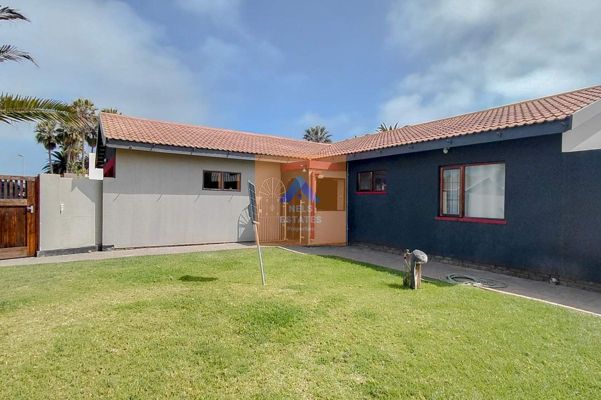 A rear view of the house featuring a tiled roof, paved walkway, and a well-maintained lawn area enclosed by boundary walls.