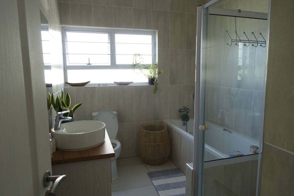 A modern bathroom featuring a vessel sink on a wooden vanity, a bathtub with a glass shower screen, and neutral wall tiling.