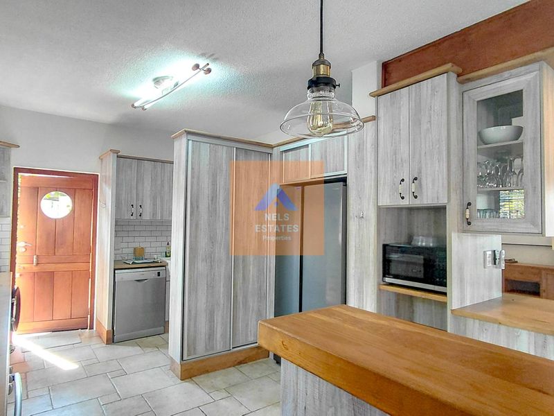 A functional kitchen featuring light wood-grain cabinetry, a wooden breakfast bar, subway tile backsplash, and modern pendant lighting with tiled flooring throughout.