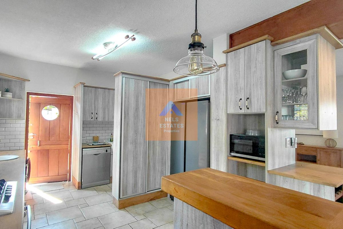 A functional kitchen featuring light wood-grain cabinetry, a wooden breakfast bar, subway tile backsplash, and modern pendant lighting with tiled flooring throughout.