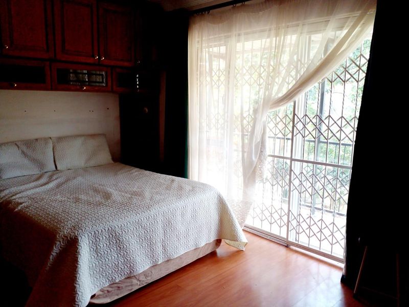 A bedroom featuring laminate flooring, built-in cabinetry, and a sliding glass door with a security gate leading to the exterior.