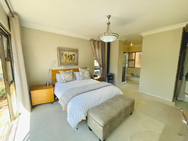 Spacious bedroom featuring neutral carpeting, cove molding, and an integrated en-suite bathroom with a sliding glass door leading to the exterior.
