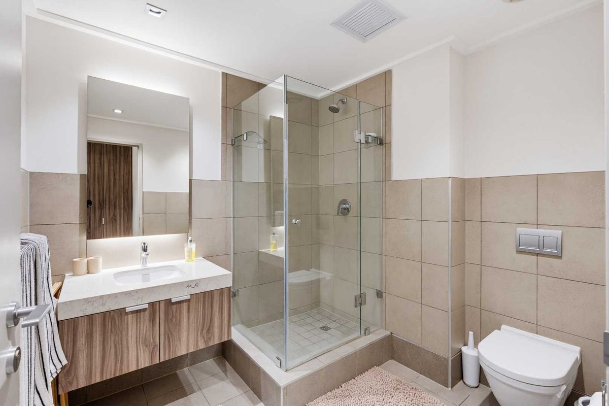 Modern bathroom featuring a glass-enclosed shower, wall-mounted vanity with stone countertop, and a wall-hung toilet with neutral tiled finishes.