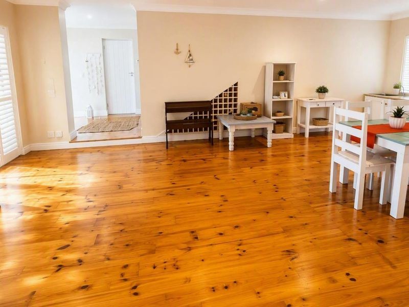 Spacious open-plan living and dining area featuring warm timber flooring, plantation shutters, and a built-in wine rack, offering a bright and inviting atmosphere.