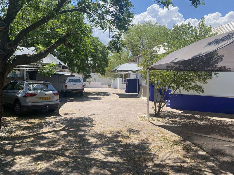 A paved rear courtyard area featuring shade cloth carports and established trees, providing functional outdoor parking space for the office property.