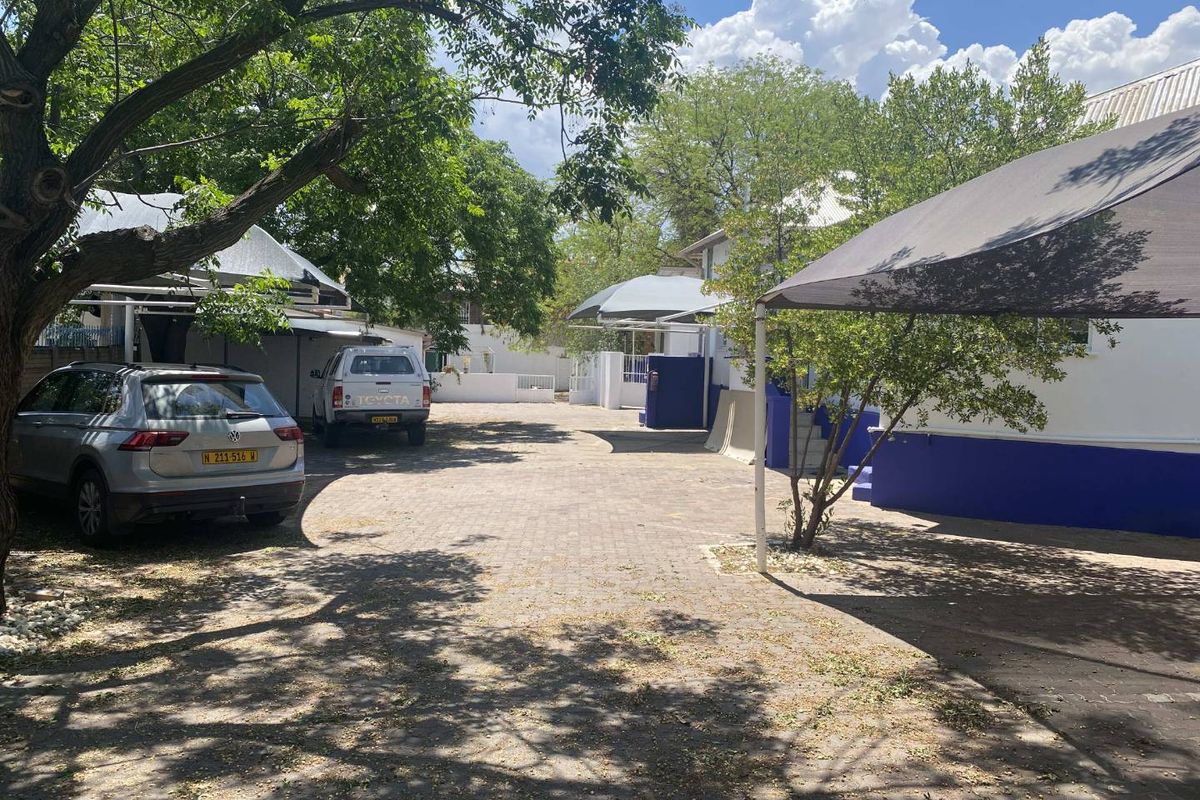 A paved rear courtyard area featuring shade cloth carports and established trees, providing functional outdoor parking space for the office property.