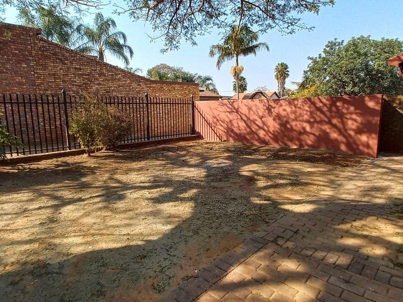 A rear garden area featuring a paved walkway, brick boundary walls, and metal security fencing.