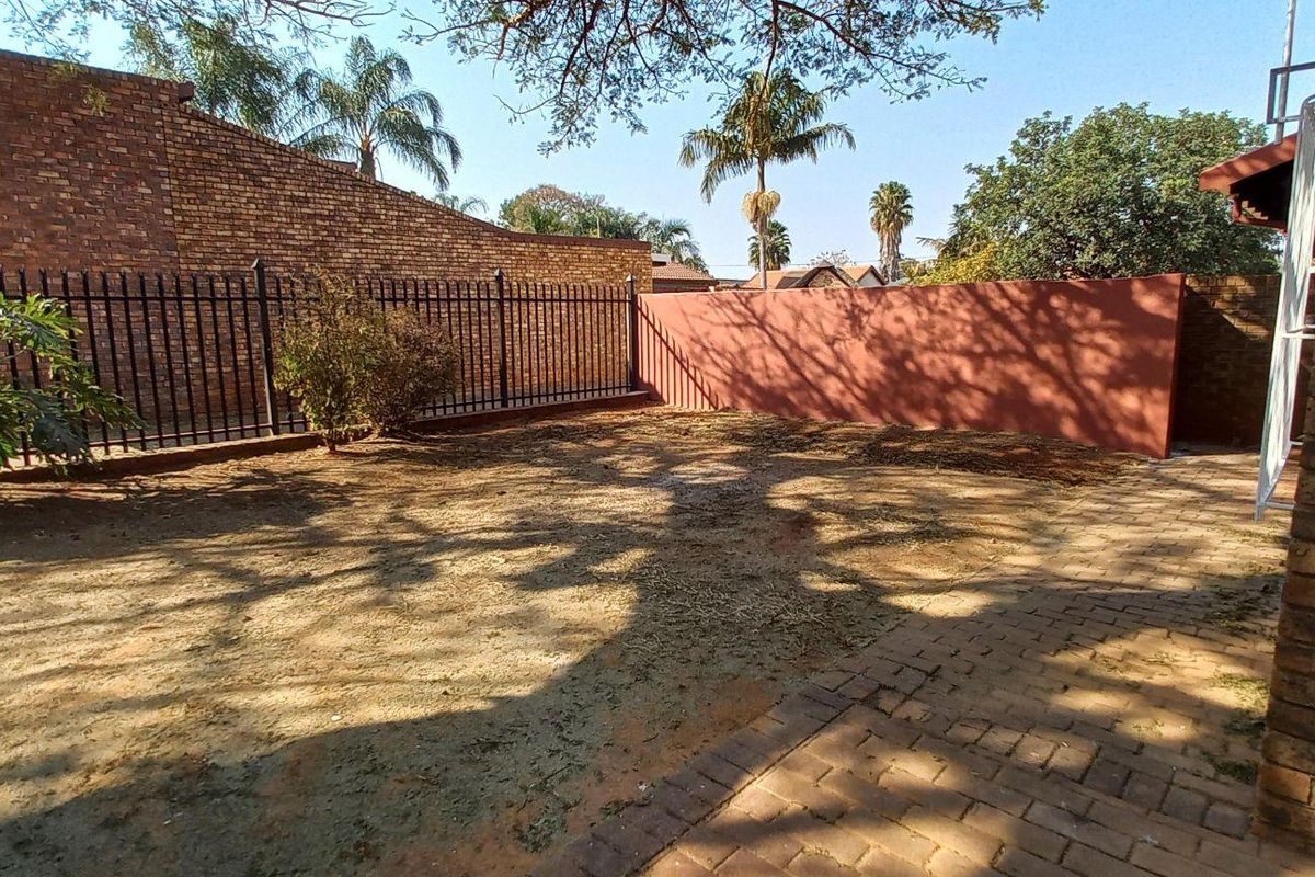 A rear garden area featuring a paved walkway, brick boundary walls, and metal security fencing.