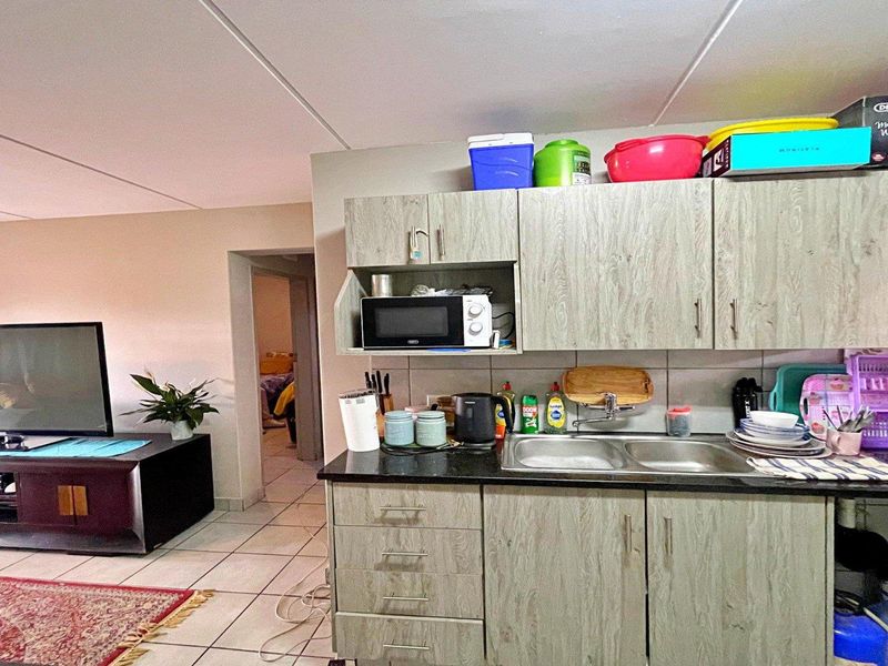Open plan living area featuring a functional kitchen with laminate cabinetry, double sink, and tiled flooring, seamlessly connecting to the adjacent living space.