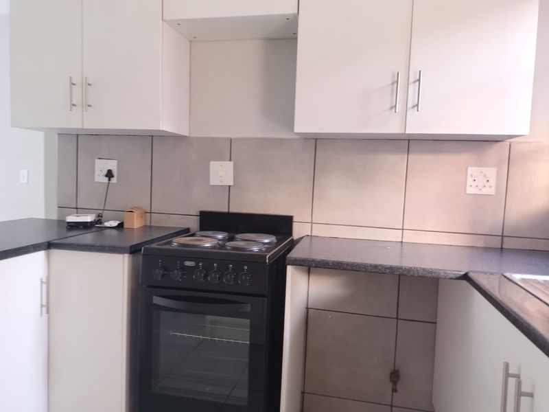 A functional kitchen featuring white built-in cabinetry, dark laminate countertops, a tiled backsplash, and a freestanding stove.