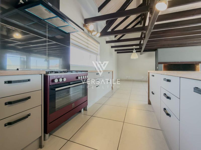 Modern kitchen featuring a gas stove, extractor fan, kitchen island, and exposed timber ceiling beams with neutral tiled flooring.